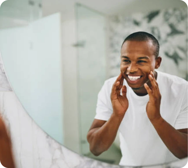 Man examining his face in a bathroom mirror with hands on cheeks